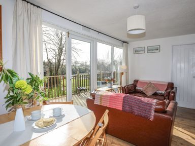 A living room with a brown leather sofa and a dining table near large glass doors opening to a wooden balcony at Treetops in Caernarfon