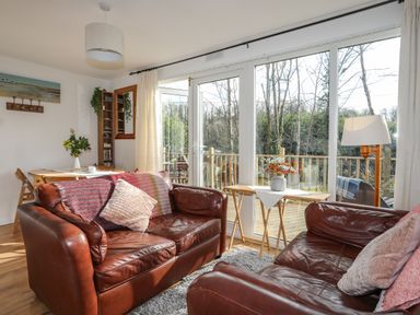 A living room with leather sofas and a table with flowers near large windows at Treetops in Caernarfon