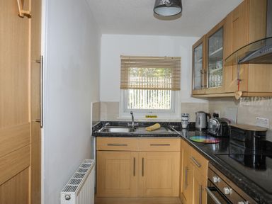 A kitchen with wooden cabinets a stainless steel sink a window blinds and small appliances at Treetops in Caernarfon
