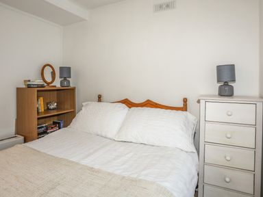 A bedroom with a bed white pillows wooden shelving unit and a white chest of drawers each with a lamp at Treetops in Caernarfon