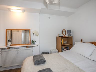 A bedroom with a bed folded towels a bookshelf a mirror a table lamp a flower and a wall light at Treetops in Caernarfon