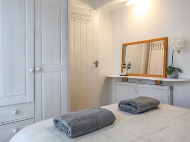 A bedroom with a white wardrobe a door a wall shelf with a mirror and two folded gray towels on a bed at Treetops in Caernarfon