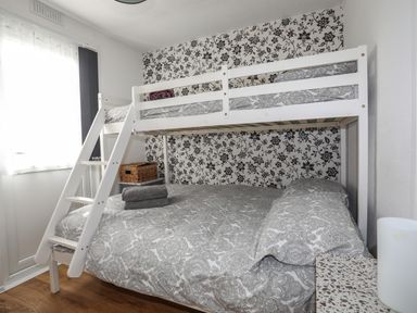 A bedroom with a white bunk bed a patterned wall and window with curtains at Treetops in Caernarfon
