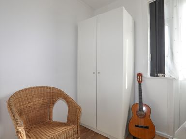 A room with a wicker chair a white wardrobe and a guitar near a window at Treetops in Caernarfon