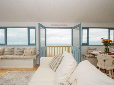 A living room with white sofa striped pillows blue doors and windows overlooking the sea at Solana in Whitsand Bay