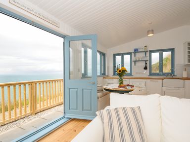 A kitchen and dining area with blue doors and windows overlooking a wooden deck and the sea at Solana in Whitsand Bay