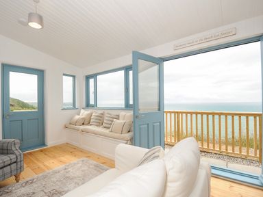 A room with light wood flooring blue doors windows and a cushioned bench facing the sea at Solana Whitsand Bay