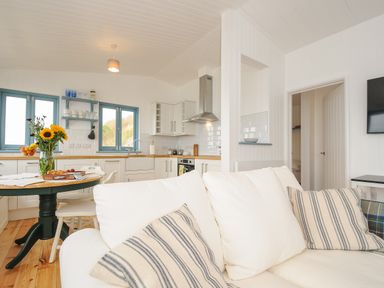 A kitchen and living area with a white sofa and striped cushions and a dining table with flowers at Solana Whitsand Bay