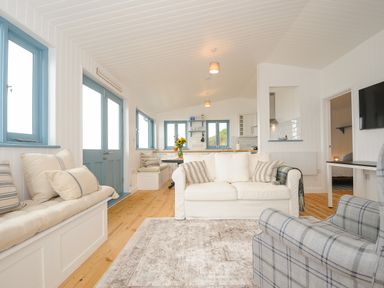 A living room with white sofa blue plaid armchair wooden floor and built in bench seating at Solana Whitsand Bay