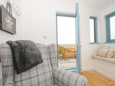 An armchair with a blanket an open door leading to a patio bench and a window seat with cushions at Solana Whitsand Bay