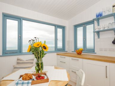 A kitchen with blue window frames wooden countertop flowers croissants and strawberries on a table at Solana in Whitsand Bay