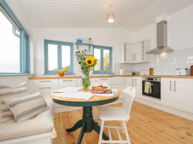 A kitchen with white cabinets wooden countertops a round table with a vase of flowers and chairs at Solana in Whitsand Bay