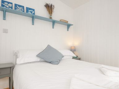 A bedroom with a white bed grey pillow blue shelf with decorations and a bedside table with a lamp at Solana Whitsand Bay