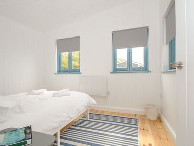 A bedroom with a bed towels on a striped rug and blue window frames at Solana in Whitsand Bay