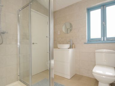 A bathroom with a shower enclosure a white sink with cabinet a round mirror a toilet and a window with blue frame at Solana in Whitsand Bay