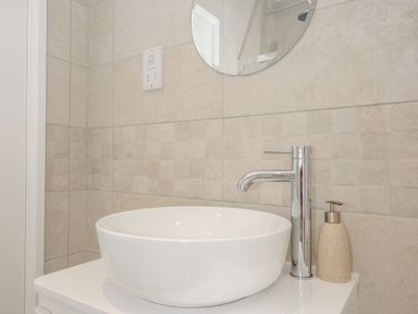 A bathroom sink with a tall faucet and a soap dispenser under a round mirror at Solana in Whitsand Bay