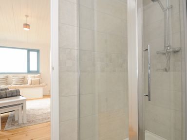 A shower area with glass door and tiled walls next to a living room with a window seat and a coffee table at Solana in Whitsand Bay