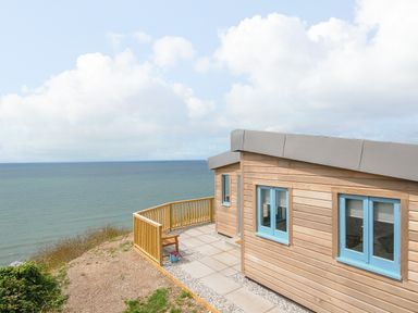 A wooden cabin with blue windows next to a patio overlooking the sea at Solana in Whitsand Bay
