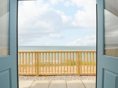A view of the ocean through open double blue doors with a wooden railing outside at Solana Whitsand Bay