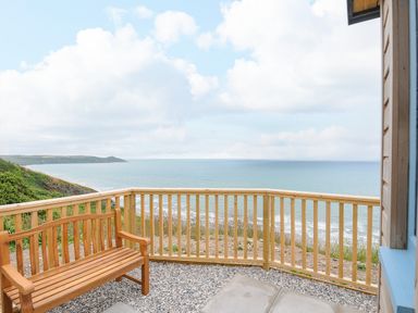 A wooden bench on a balcony with a wooden railing overlooking the sea and cliffs at Solana in Whitsand Bay