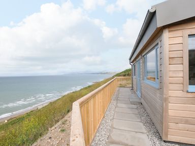 A wooden cabin with a stone path and wooden railing overlooking the ocean at Solana in Whitsand Bay