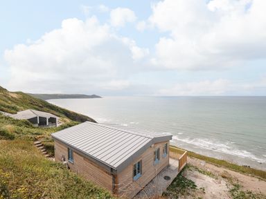 A wooden cabin on a hillside overlooking the ocean with another cabin in the distance at Solana in Whitsand Bay