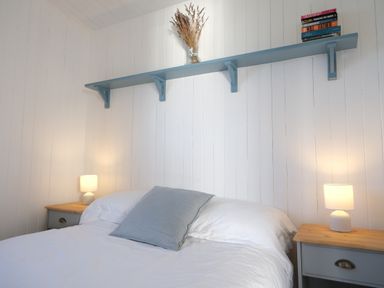 A bedroom with a bed and nightstands with lamps and a shelf with books and flowers at Solana Whitsand Bay