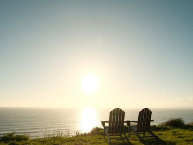 Two wooden chairs facing the ocean with the sun low in the sky at Solana in Whitsand Bay