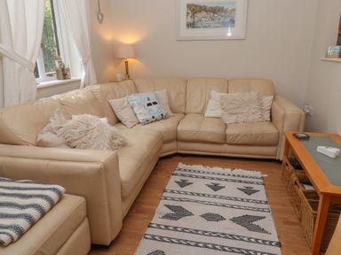 A living room with a beige corner sofa, cushions, a patterned rug, a side table with a lamp, and a wooden coffee table at Alberts Den in Falmouth