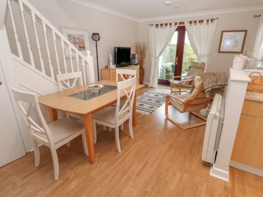 A dining area with a wooden table and white chairs next to a living space with armchairs a television and glass doors at Alberts Den in Falmouth