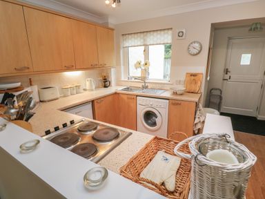 A kitchen with wooden cabinets a stove a washing machine and a window with flowers at Alberts Den in Falmouth