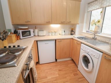 A kitchen with wooden cabinets a microwave toaster kettle washing machine and sink at Alberts Den in Falmouth