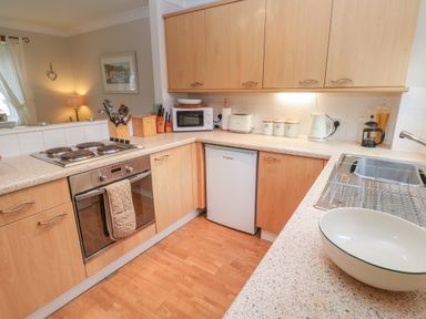 A kitchen with wooden cabinets electric stove oven microwave toaster kettle and sink at Alberts Den in Falmouth