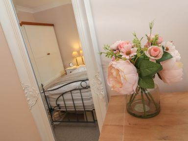 A vase with pink flowers on a wooden surface next to a mirror reflecting a bedroom at Alberts Den in Falmouth