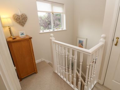 A staircase with white banisters next to a window and a wooden cabinet with a lamp at Albert's Den in Falmouth