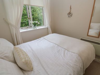 A bedroom with a bed near a window with white curtains and flowers at Albert's Den in Falmouth