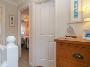 A hallway with a wooden dresser and an open door leading to a bedroom at Alberts Den in Falmouth