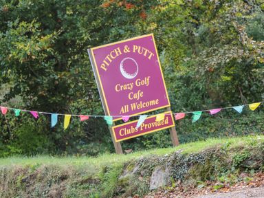 A pitch and putt sign with colorful flags in front of trees at Alberts Den in Falmouth