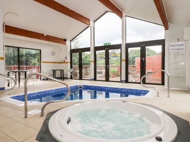An indoor pool area with a hot tub and a pool surrounded by metal handrails and tables with chairs at Albert's Den in Falmouth