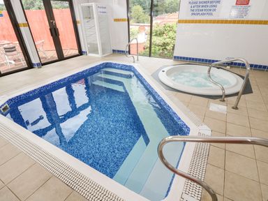 An indoor pool and a hot tub in a tiled room with large windows and a sign on the wall at Albert's Den in Falmouth