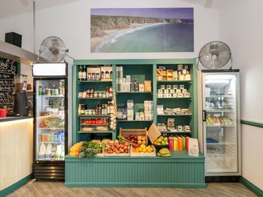 A small shop with shelves of food items fresh fruit and vegetables and two refrigerated display cases at Alberts Den in Falmouth