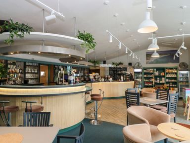 An interior of a cafe with a curved bar counter bar stools shelves with products and seating area at Alberts Den in Falmouth