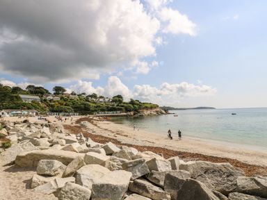 A sandy beach with rocks in the foreground and houses on a green hillside at Albert's Den in Falmouth