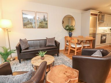 A living room with brown leather sofa and chairs a wooden coffee table a dining table with chairs and a kitchen in the background at Reubens Cottage in Fremington Devon