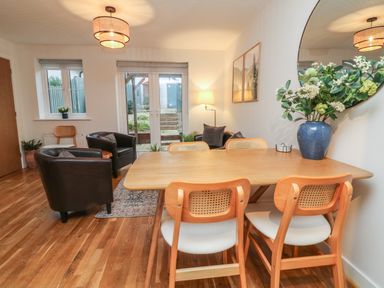 A dining and living area with wooden table and chairs leather armchairs and a glass door at Reubens Cottage in Fremington Devon