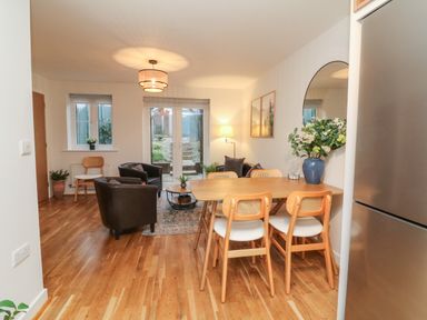 A dining area with wooden table and chairs next to a living room with armchairs and a sofa at Reubens Cottage in Fremington Devon