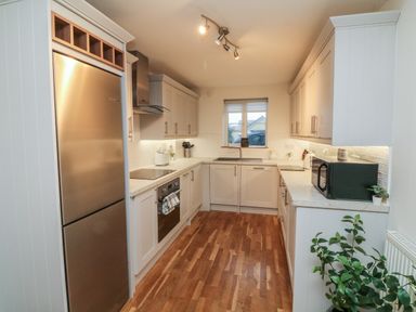 A kitchen with wooden floor cabinets microwave refrigerator oven a window and plants at Reubens Cottage in Fremington Devon