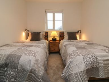 A bedroom with two single beds a wooden nightstand with a lamp and a window at Reubens Cottage in Fremington Devon