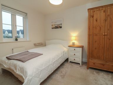 A bedroom with a bed a bedside table with a lamp a wooden wardrobe and a window at Reubens Cottage in Fremington Devon