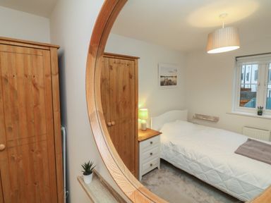 A bedroom with a bed bedside table lamp wooden wardrobes and window at Reubens Cottage in Fremington Devon